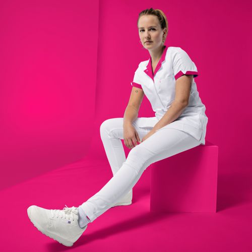 A carer is wearing white trousers and a white and pink tunic.